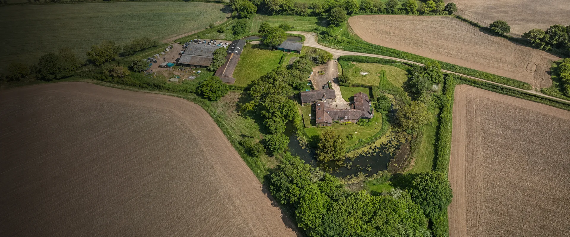 Aerial view of a rural property with farmhouse, outbuildings, pond, driveway and surrounding farmland for farm and estate surveys